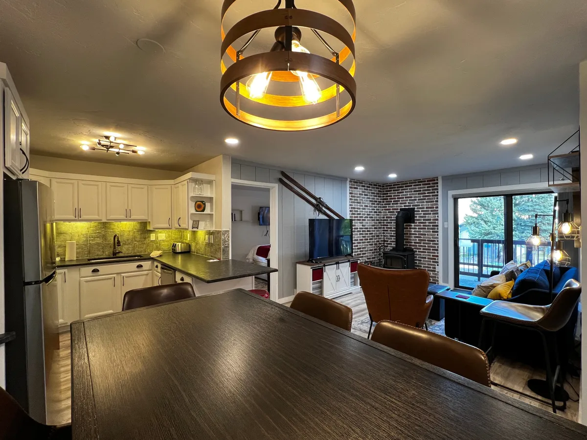 An inviting open-concept space combining the kitchen island, dining table, and seating area. A large window lets in natural light, and the layout encourages a seamless flow from cooking to dining to relaxation, ideal for family conversations and shared stories.