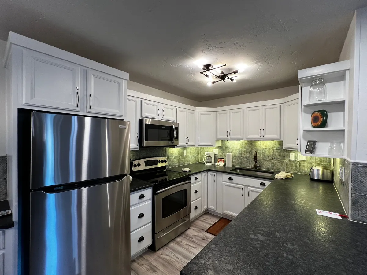 A modern kitchen featuring stainless steel appliances, dark countertops, and crisp white cabinetry. The setup hints at a space ready for both quick breakfasts and elaborate group cooking sessions. Subtle signs of activity—such as baking trays and serving platters—suggest a welcoming hub for gatherings.